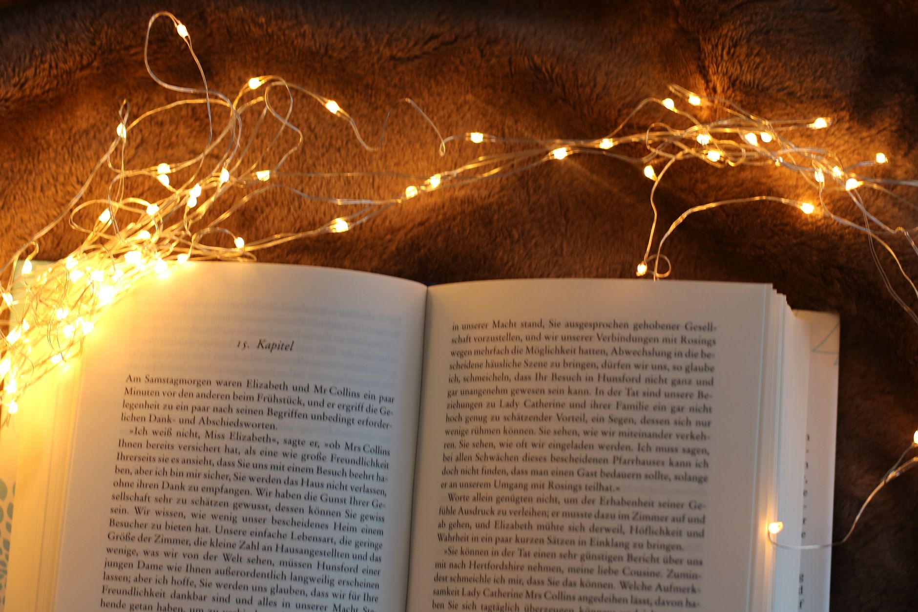 Offenes Buch, umgeben von warmen Lichterketten, die eine gemütliche Leseatmosphäre schaffen.