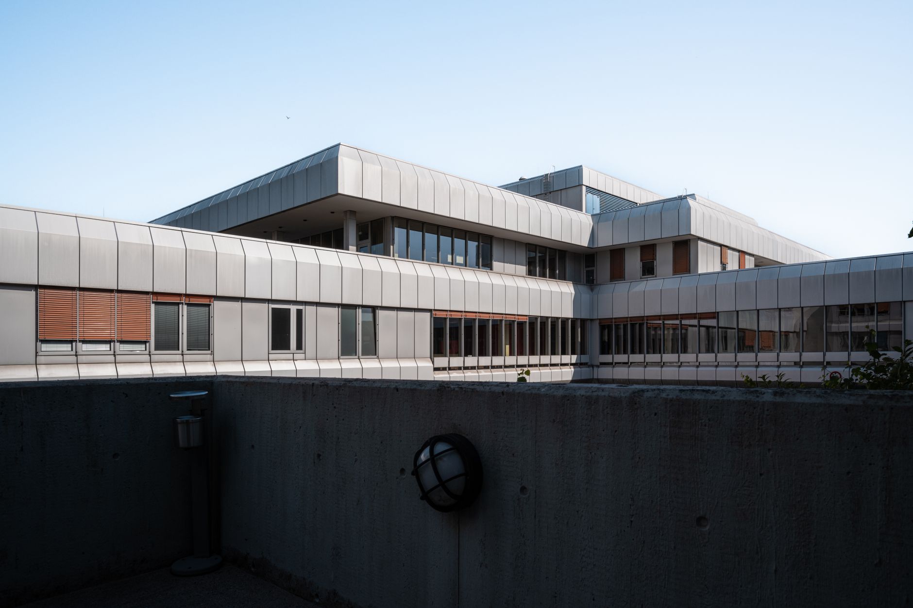 Schrägansicht eines modernen Gebäudes mit Metallfassade und großen Fenstern, unter einem klaren Himmel.