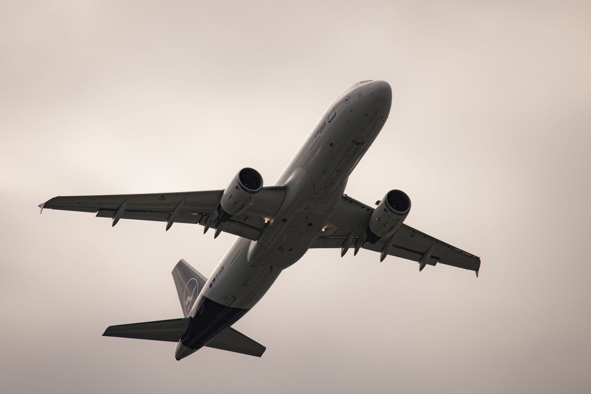 Flugzeug von unten gesehen, startet am Flughafen München unter bewölktem Himmel.