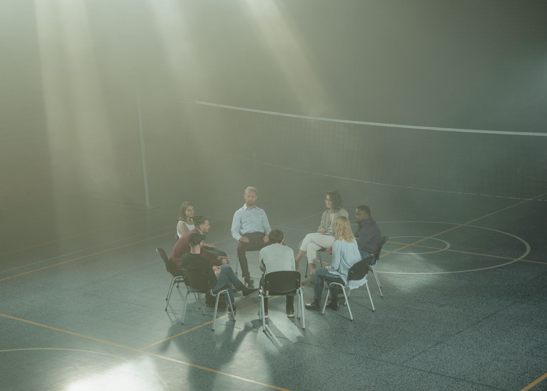 Eine diverse Gruppe versammelt sich in einem Fitnessstudio zu einer unterstützenden Therapiesitzung, mit Sonnenlicht, das durch den Dunst strömt.