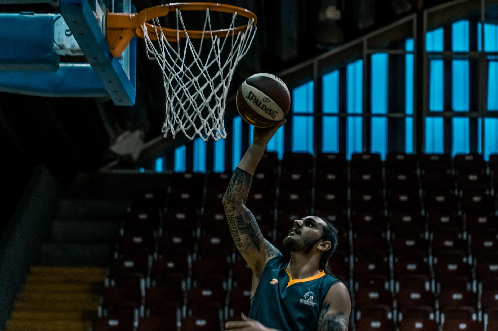 Ein fokussierter Basketballspieler erzielt einen Punkt auf einem schwach beleuchteten Innenplatz und zeigt sportliches Talent.