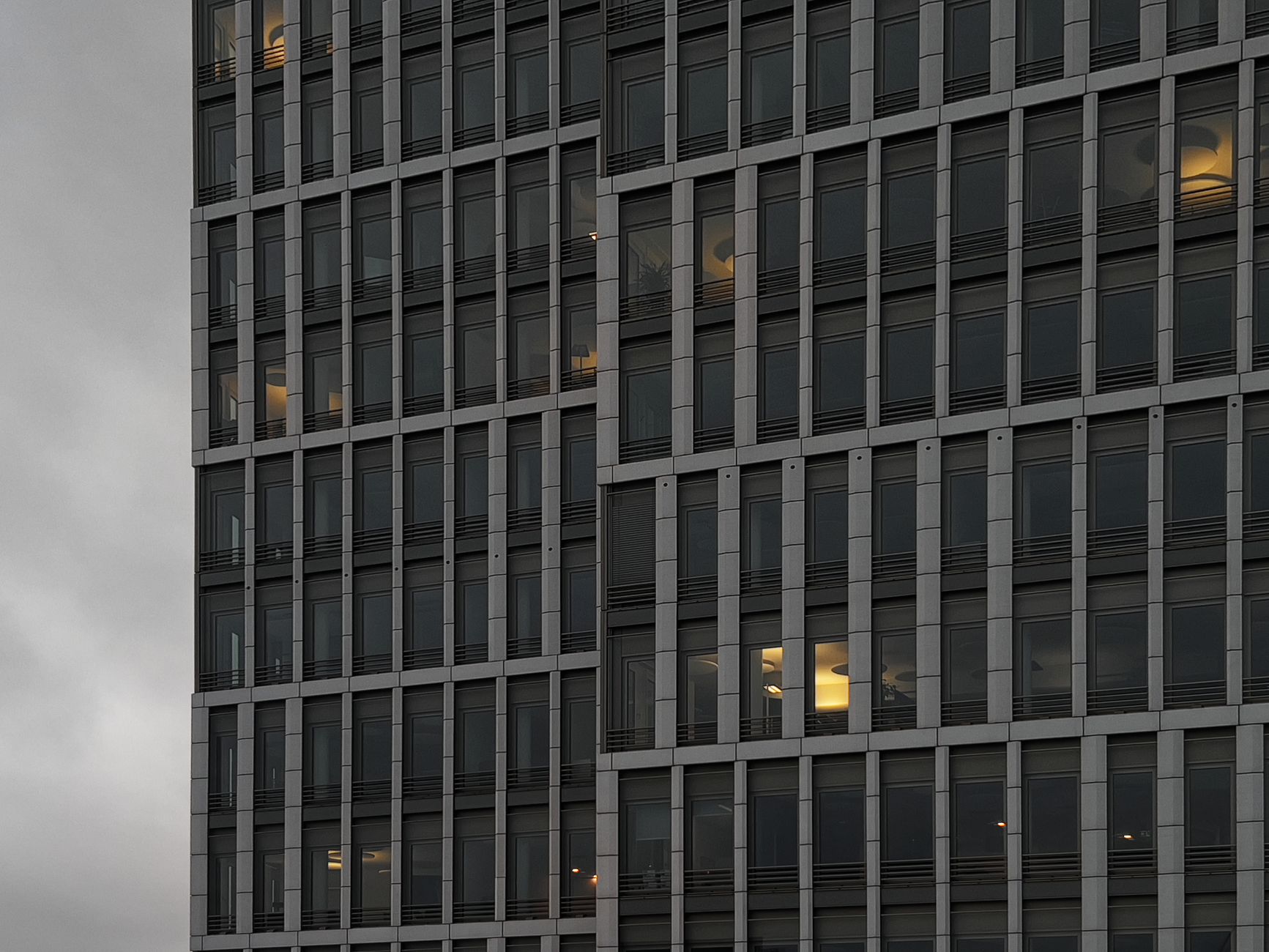 Nahaufnahme einer modernen Bürogebäudefassade mit leuchtenden Lichtern, die durch die Fenster in der Dämmerung sichtbar sind.