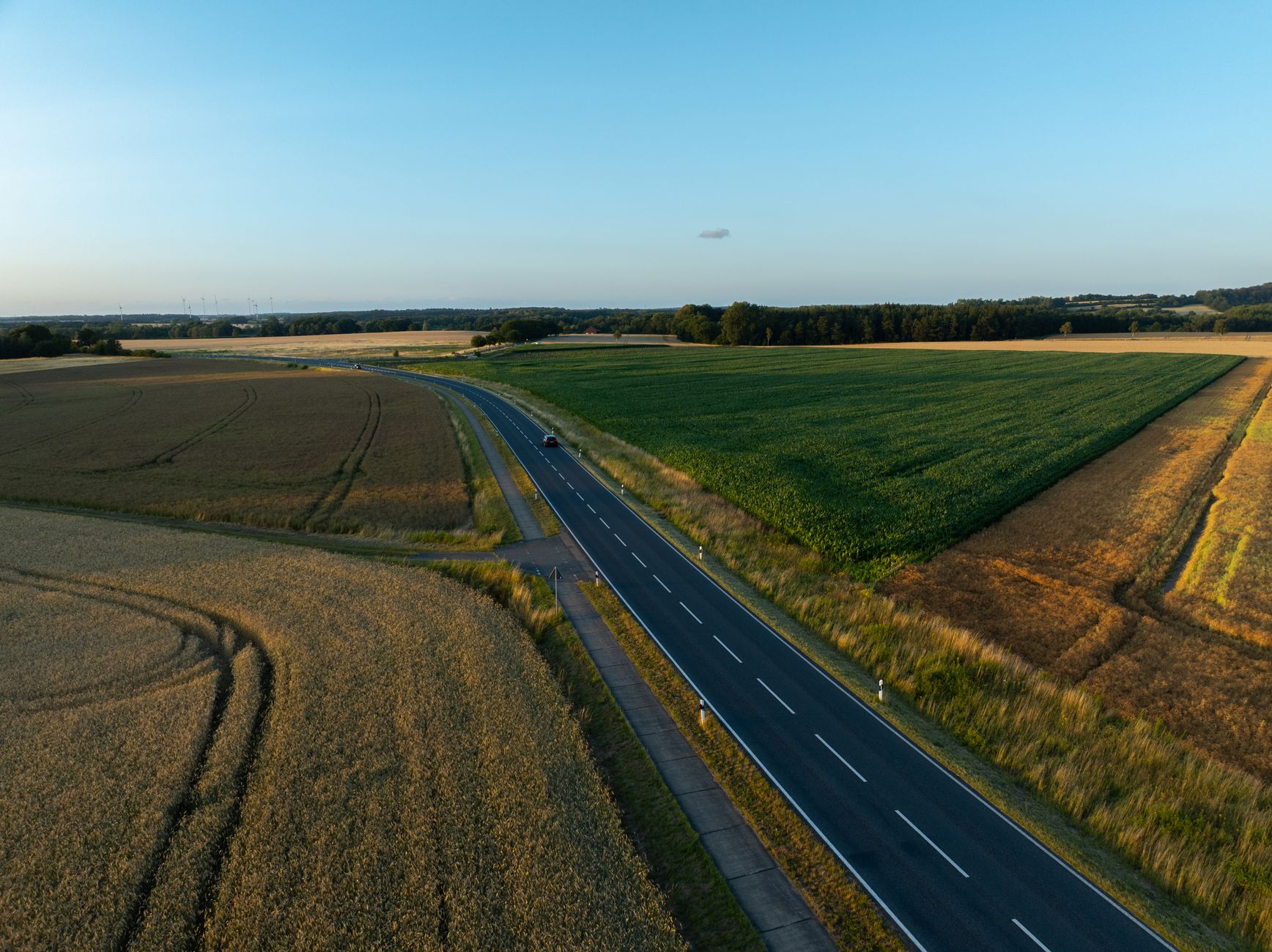 Luftaufnahme, die eine malerische Landstraße umgeben von Feldern an einem klaren Sommertag zeigt.