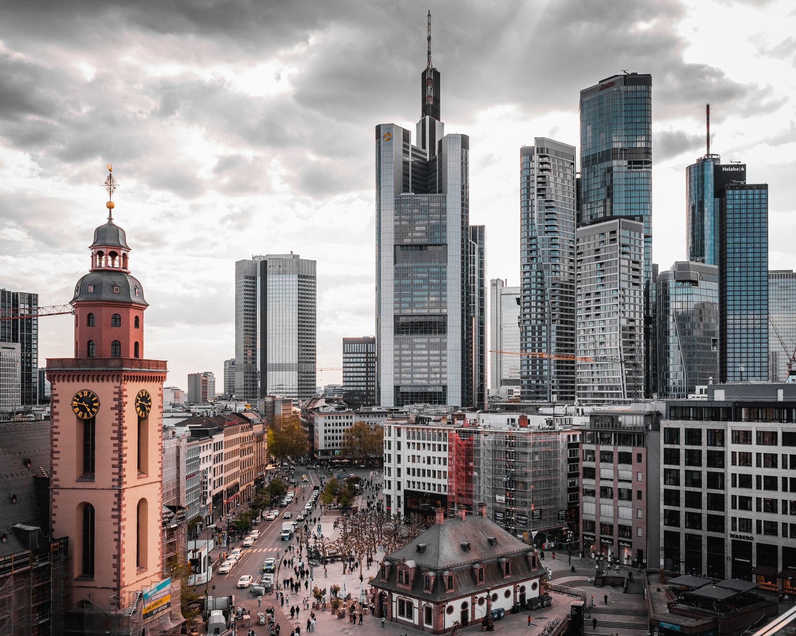 Ein atemberaubender Blick auf Frankfurts Wolkenkratzer und die historische Kirche unter einem bewölkten Himmel.