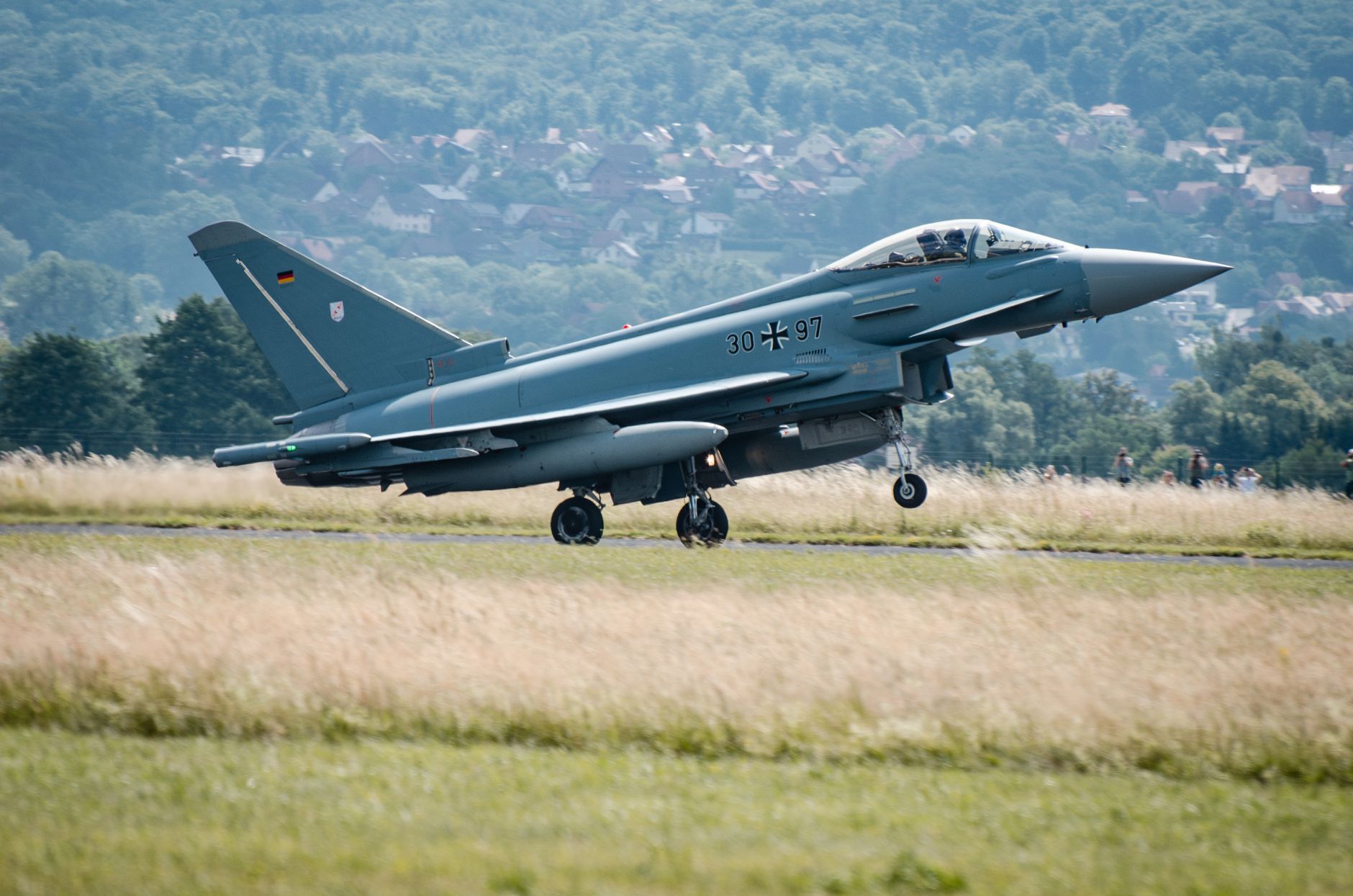 Ein Eurofighter Typhoon hebt an einem Sommertag mit malerischen Hügeln im Hintergrund ab.