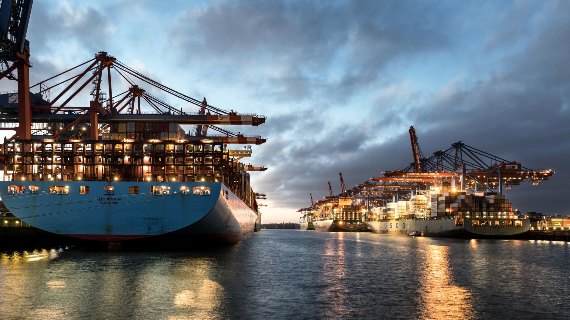 Eine malerische Ansicht von Containerschiffen, die im Hamburger Hafen während der Dämmerung liegen und das geschäftige Frachtterminal hervorheben.