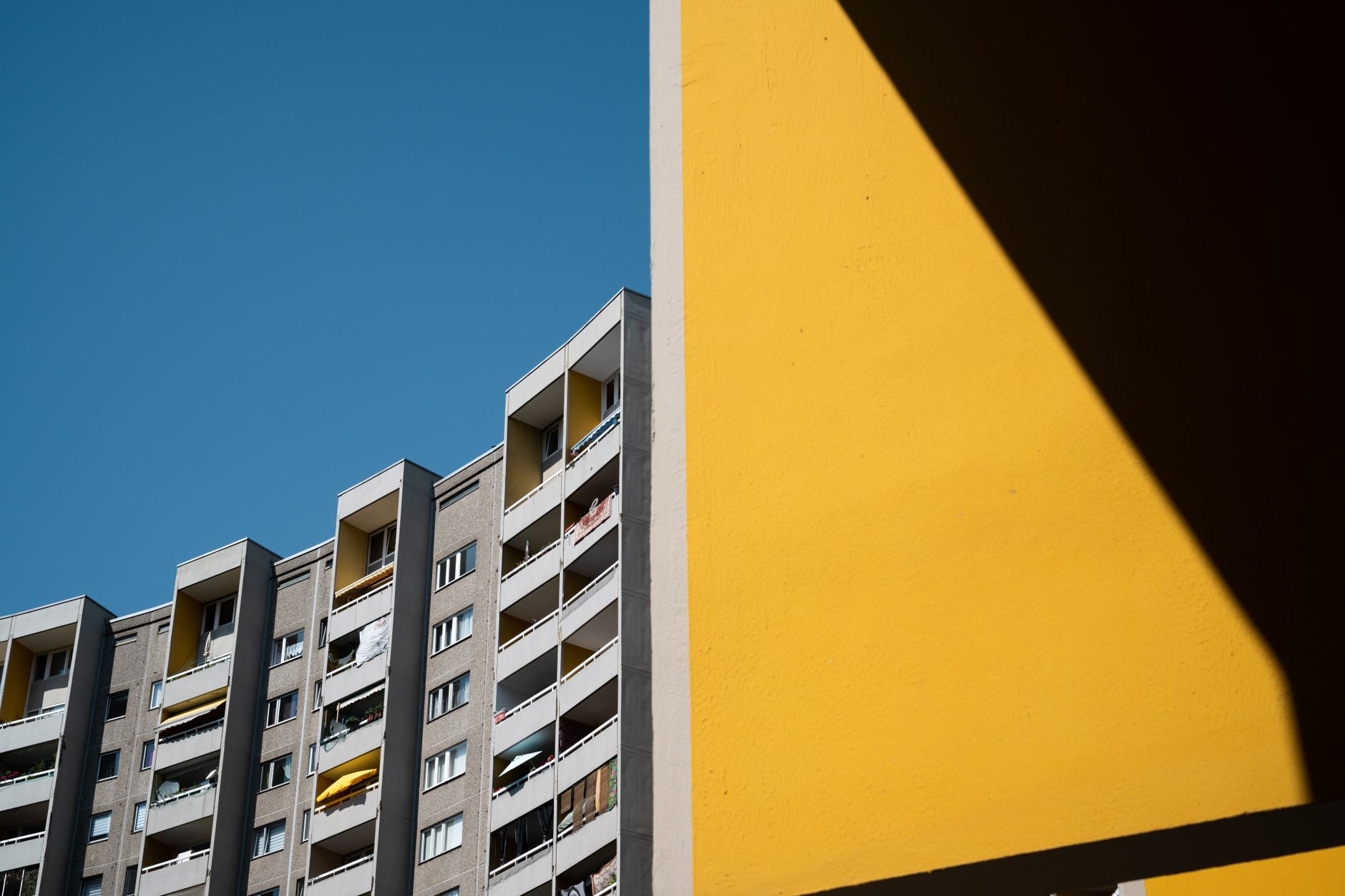 Ein minimalistisches Foto von modernen Hochhauswohnungen mit blauem Himmel und einer kräftigen gelben Wand.