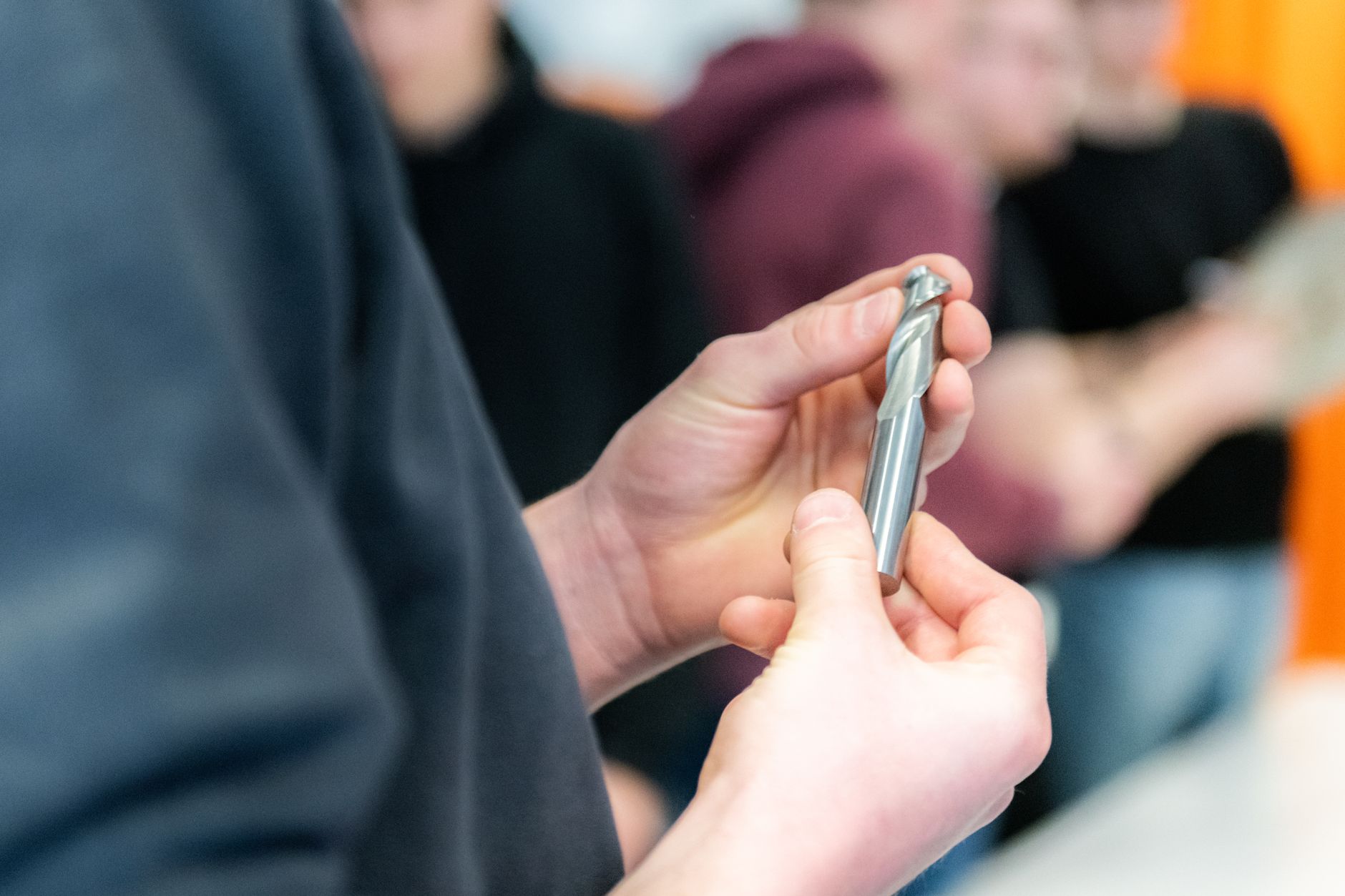 Hände, die während einer Werkstattsitzung sorgfältig einen Metallbohrer überprüfen.