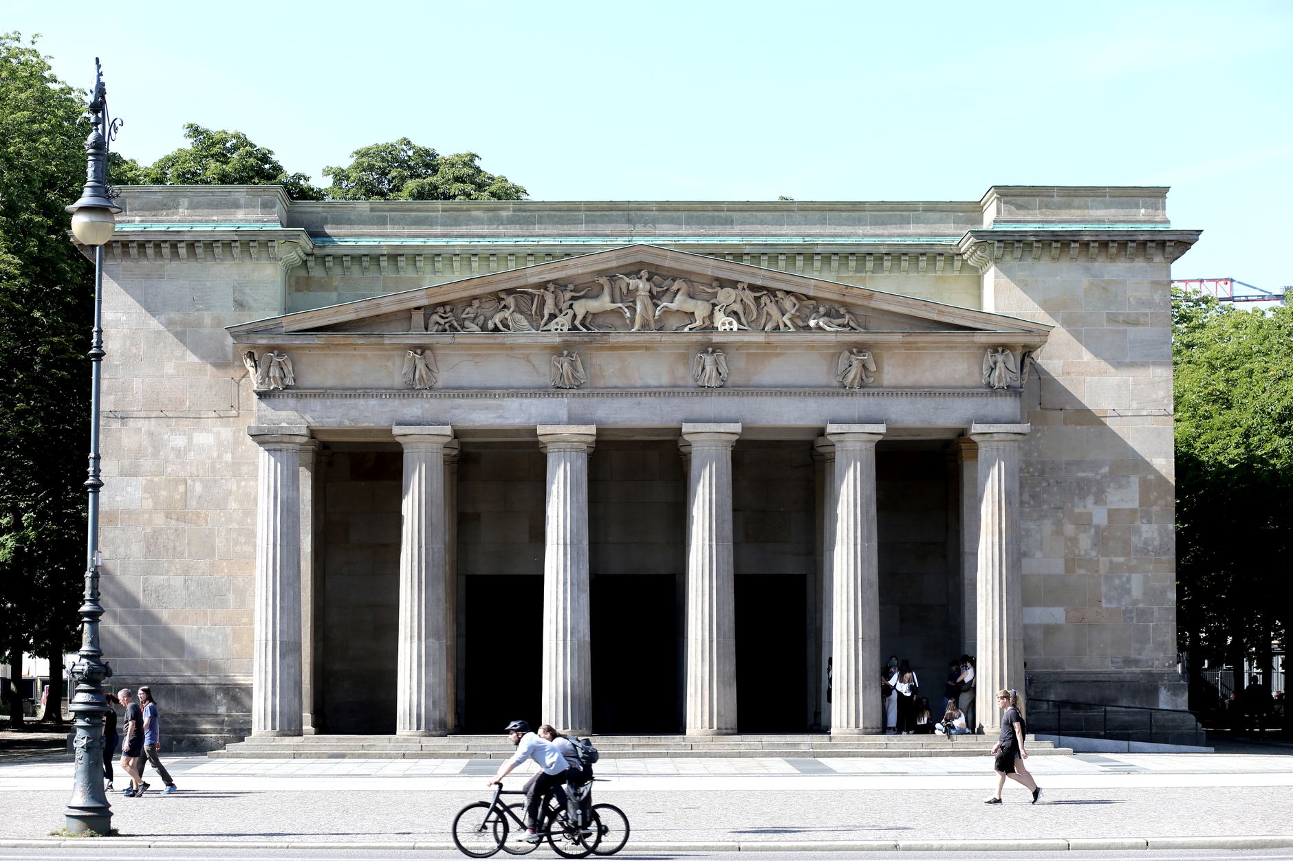 Vorderansicht der Neuen Wache in Berlin mit Passanten an einem sonnigen Tag.