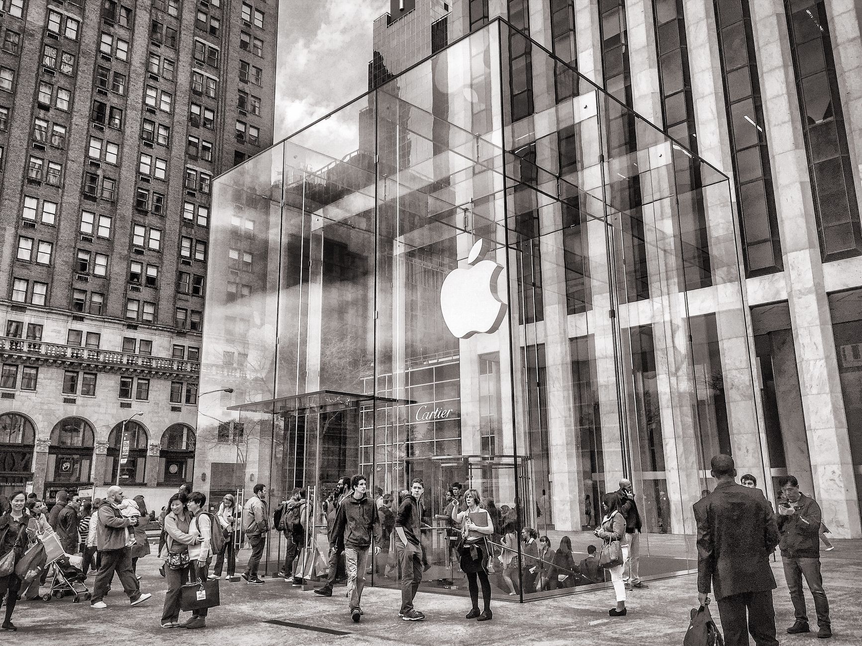 Schwarzweißfoto des geschäftigen Apple Store an der 5th Avenue in New York City mit seinem ikonischen Glaskubuseingang.