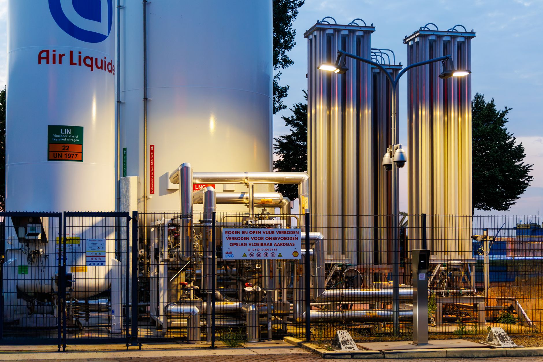 Beleuchtete Industriegasanlage in Rotterdam, die Ausrüstung und Tanks vor dem Hintergrund der Abenddämmerung präsentiert.