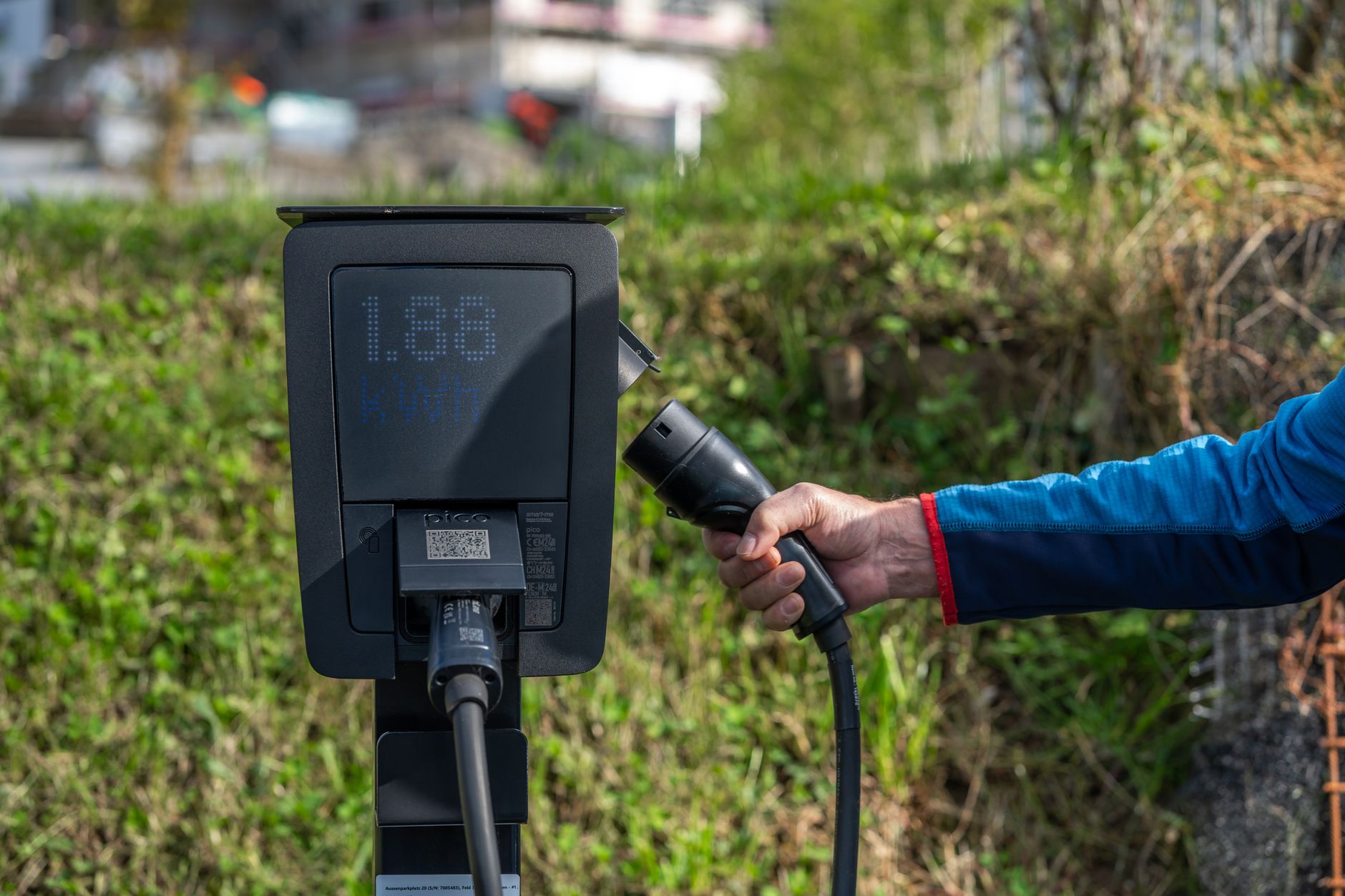 Eine Ladestation für Elektrofahrzeuge im Freien mit einer Hand, die ein Ladekabel hält.