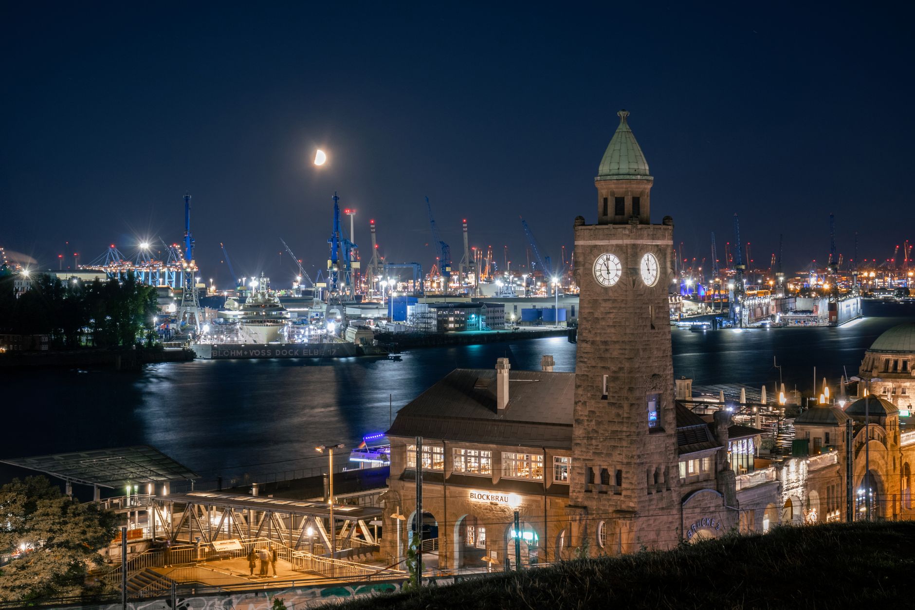  Atemberaubende nächtliche Stadtansicht des Hamburger Hafens, beleuchtet mit einem historischen Uhrturm am Wasser.