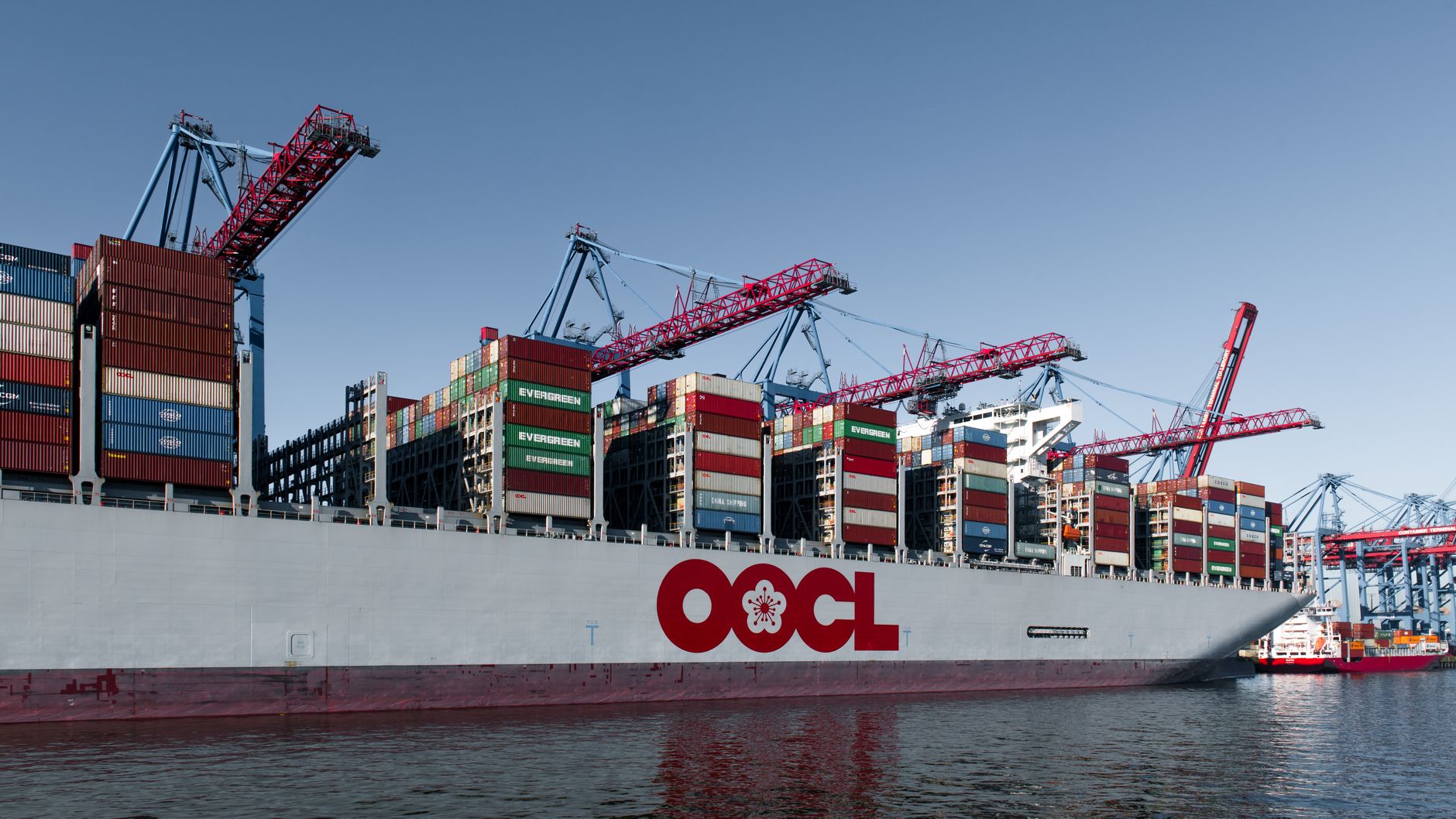 Riesiges Frachtschiff beladen mit Containern im Hamburger Hafen unter strahlend blauem Himmel.