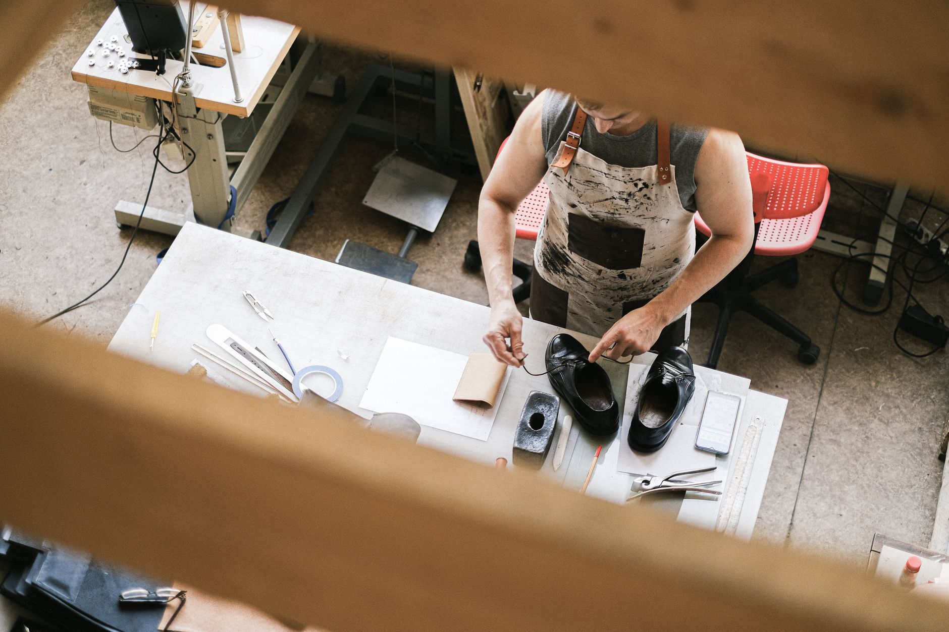 Blick von oben auf einen Ledermacher bei der Arbeit in einer Werkstatt, der sich auf die Schuhherstellung konzentriert.