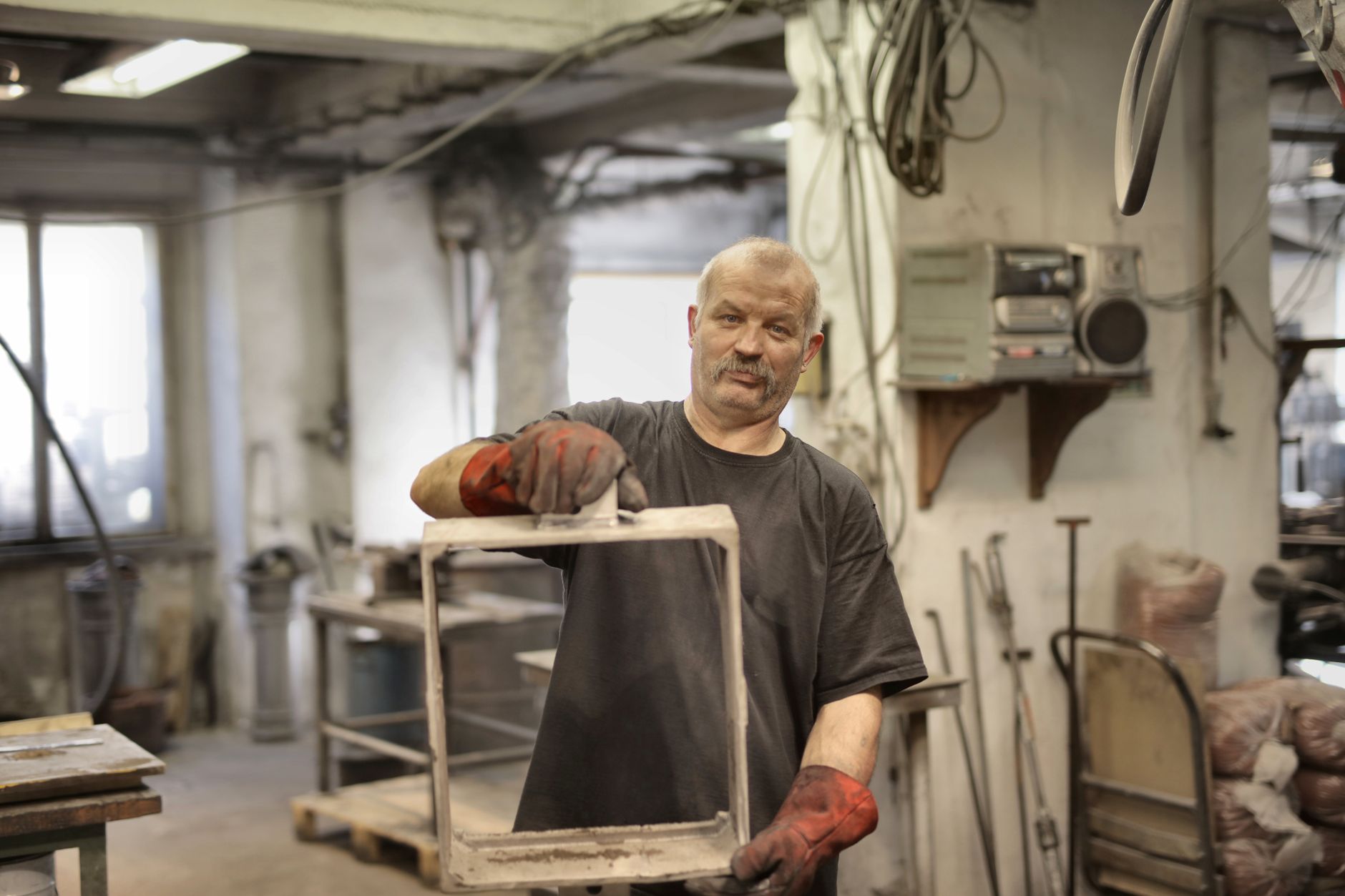 Älterer männlicher Handwerker zeigt einen Metallrahmen in einer industriellen Werkstattumgebung.